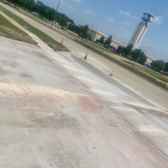 Slanted view of an airport runway with orange cones, grassy edges, and a control tower in the distance