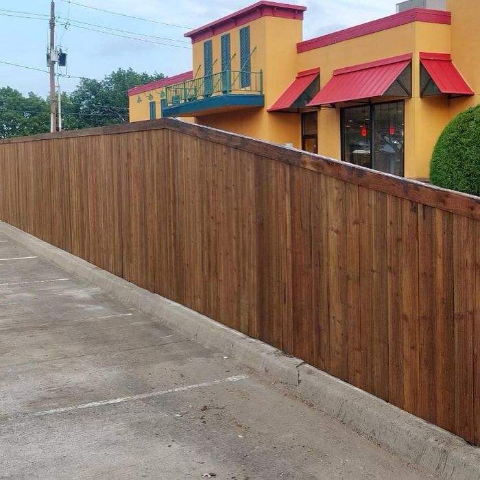 Wooden privacy fence along a concrete sidewalk beside a colorful yellow-and-red building