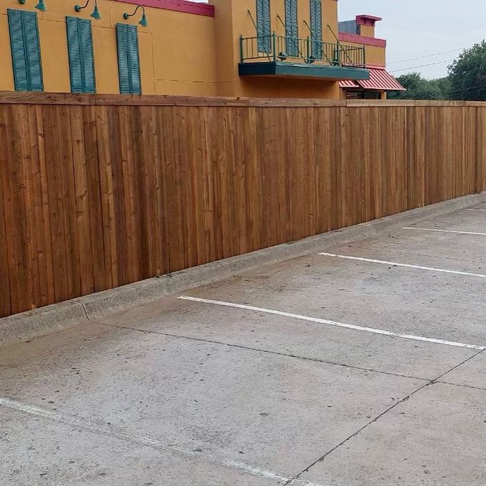 Wooden fence beside an empty concrete parking lot in front of a yellow building
