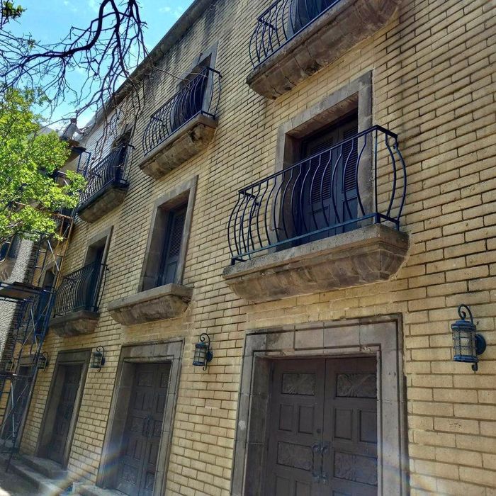 Sunlit brick apartment facade with wrought-iron balconies and a doorway, viewed from below