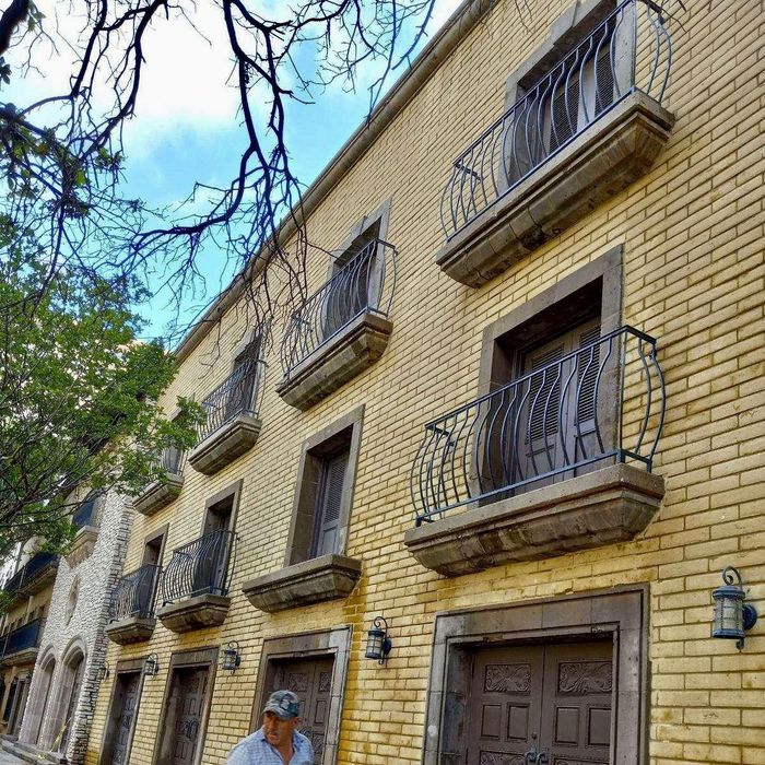 Tan brick apartment building with wrought-iron balconies and a person at the entrance