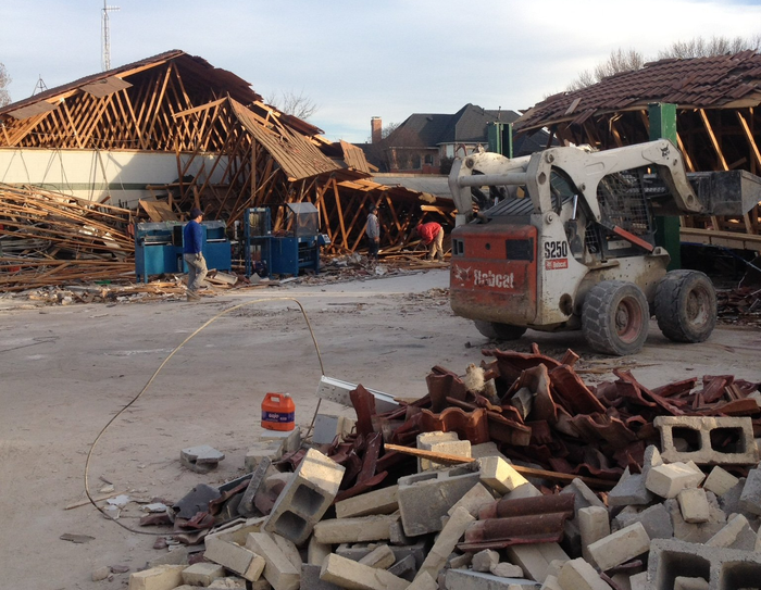Damaged houses and debris after a storm, with a forklift in the foreground.