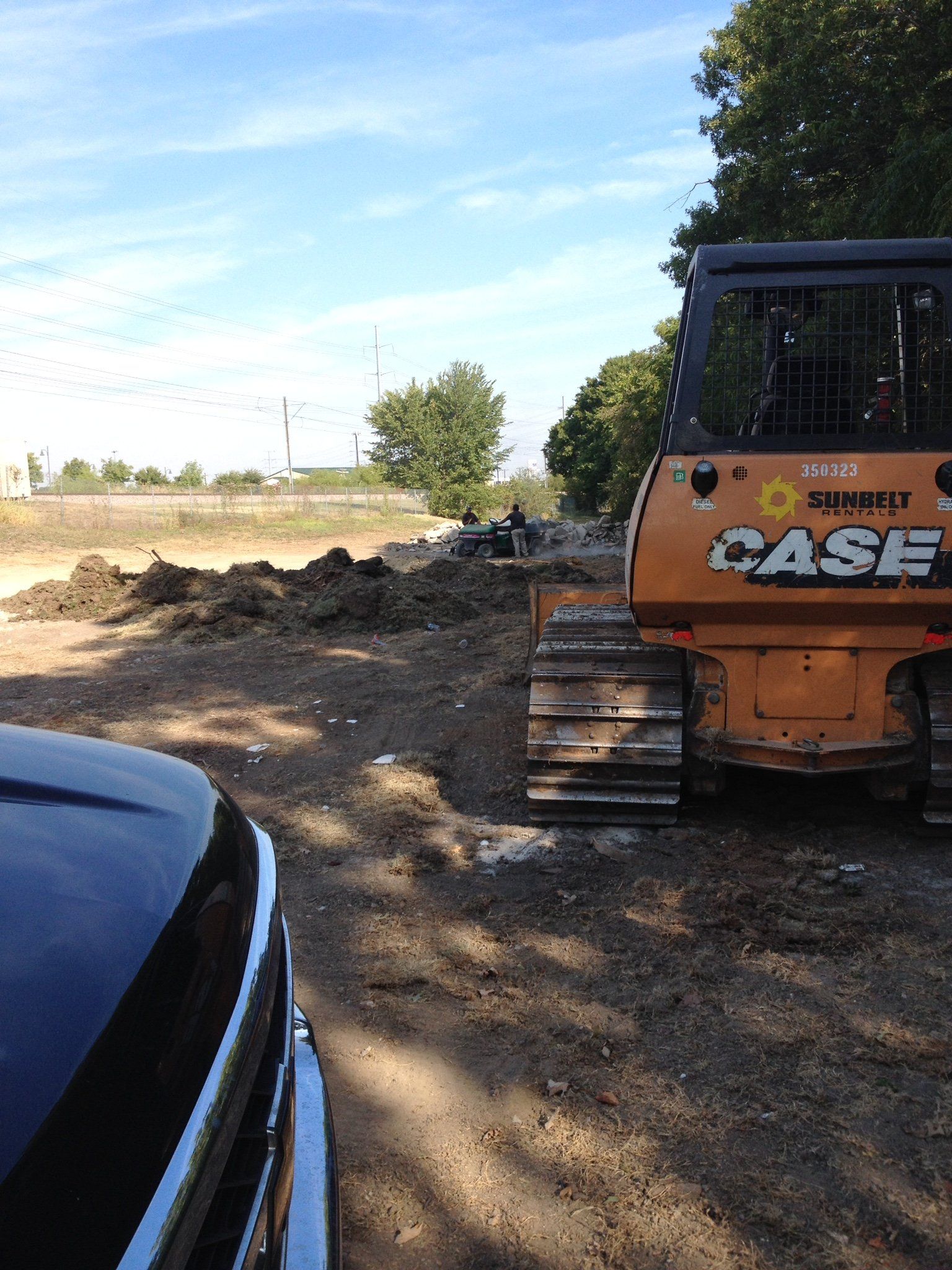 Orange CASE bulldozer beside a dirt pile on a rural worksite, with a car hood at left.