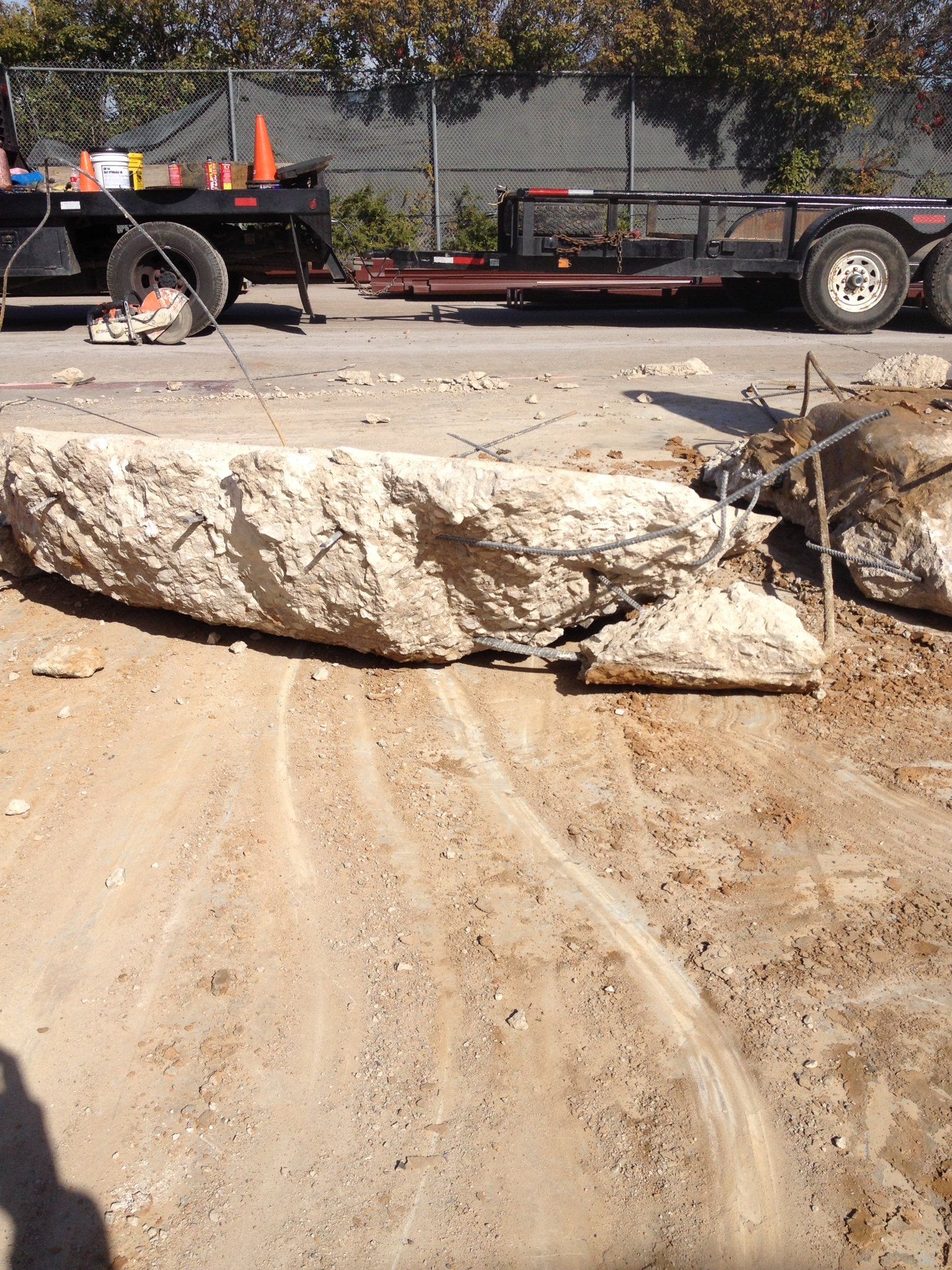 Large white boulder blocking a dirt road beside a utility trailer and cones outdoors