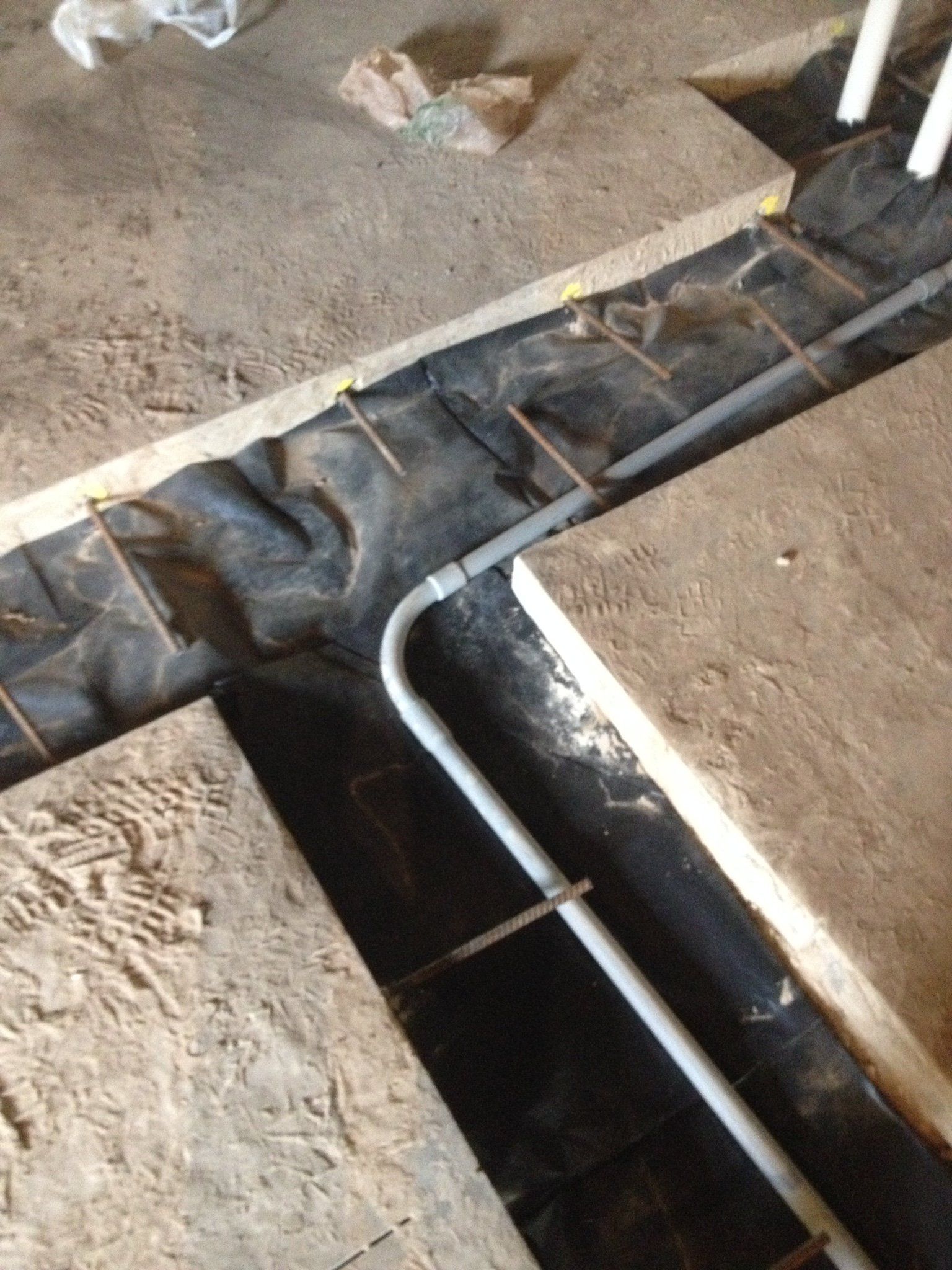 Open floor trench lined with black plastic and metal conduit on a construction site