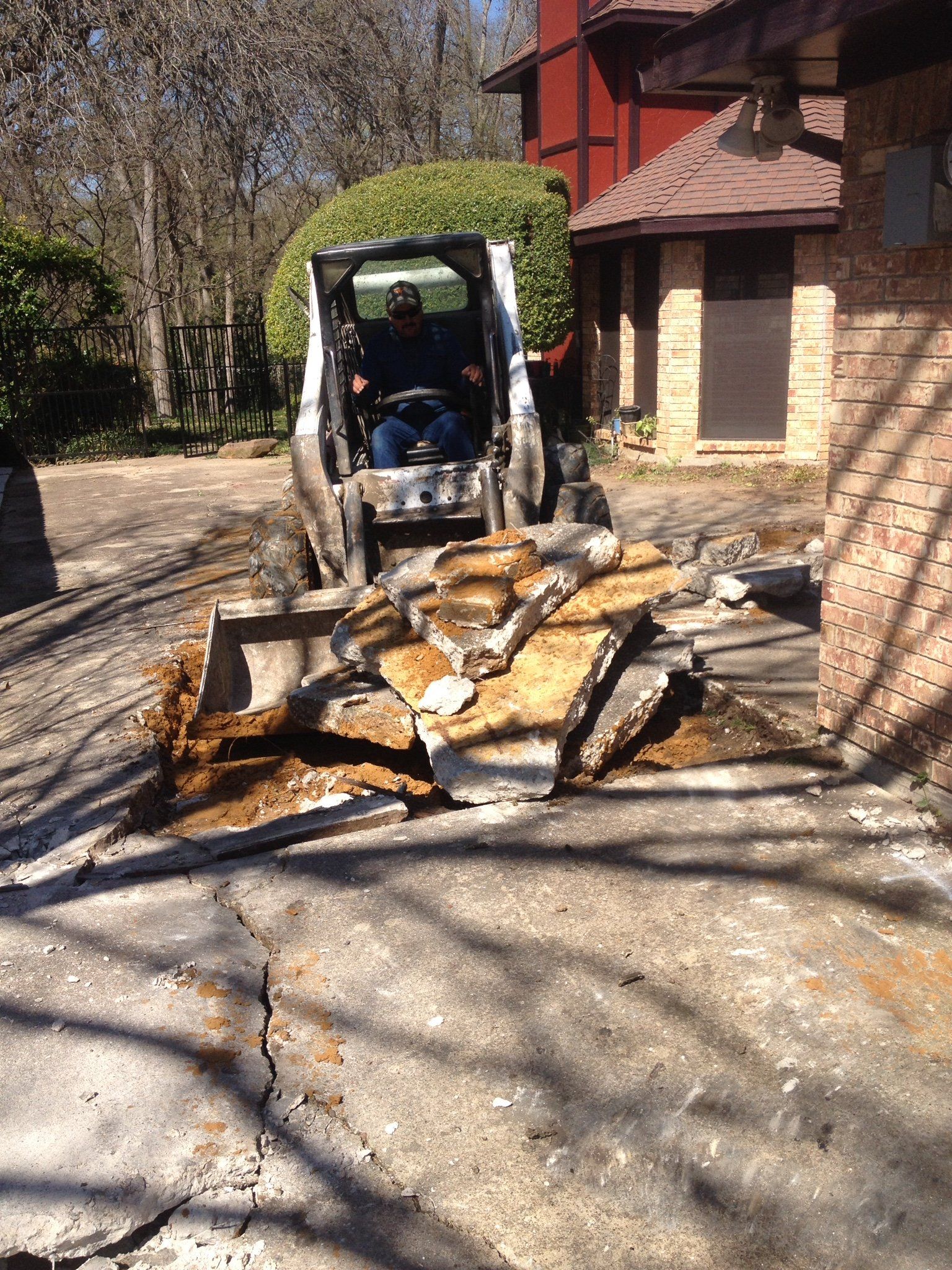 Loader pushing a pile of broken stone or concrete slabs on a driveway beside a house.
