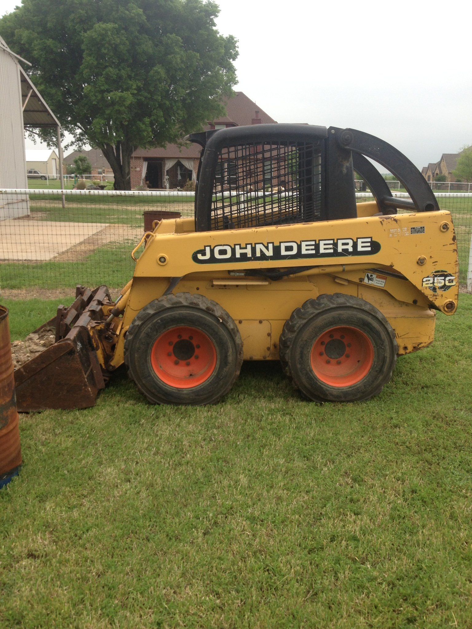 Yellow John Deere skid steer with bucket on grass near a house, side view