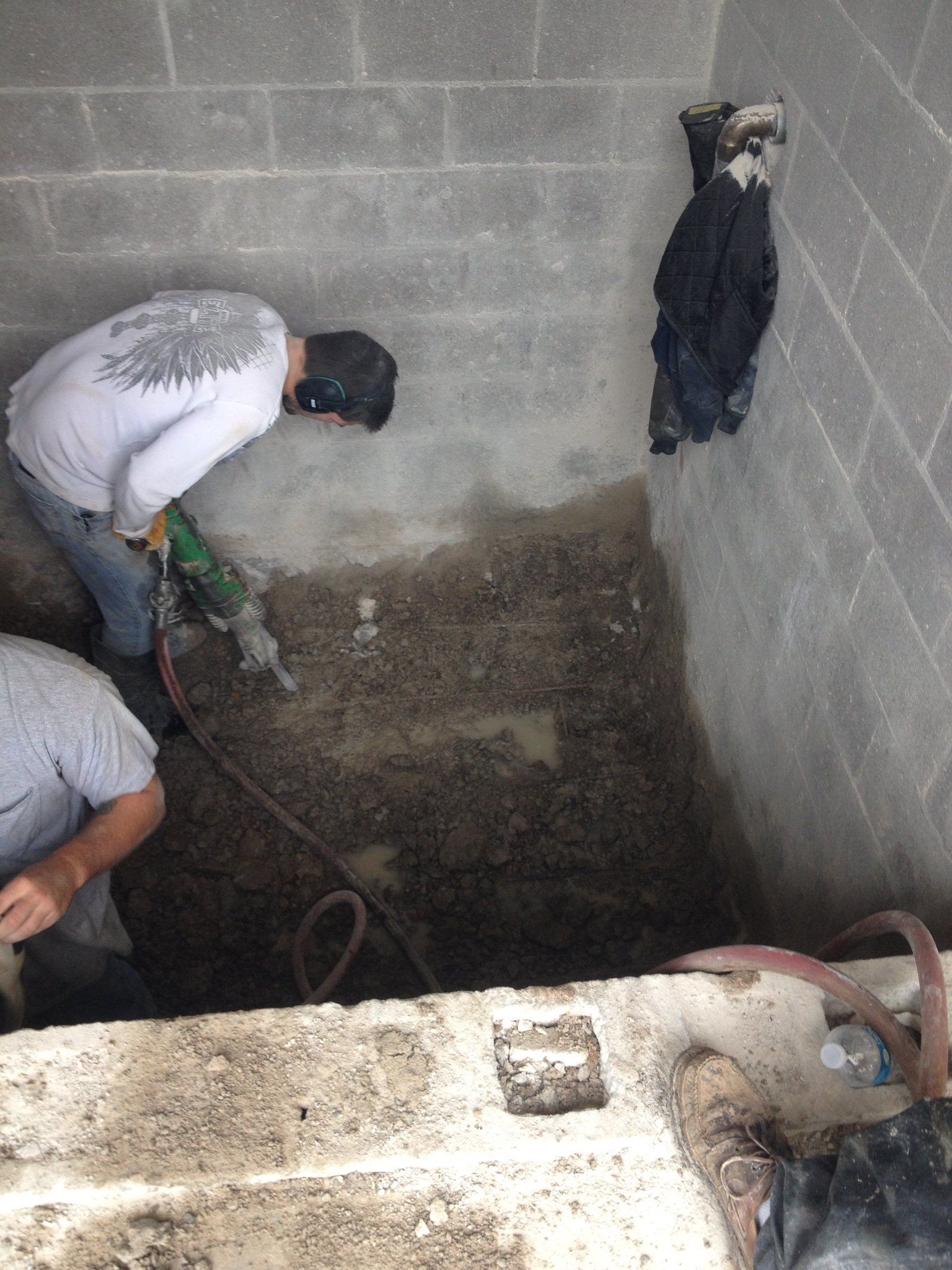 Workers cleaning a dark concrete pit beside a cinderblock wall, with hoses and tools visible.