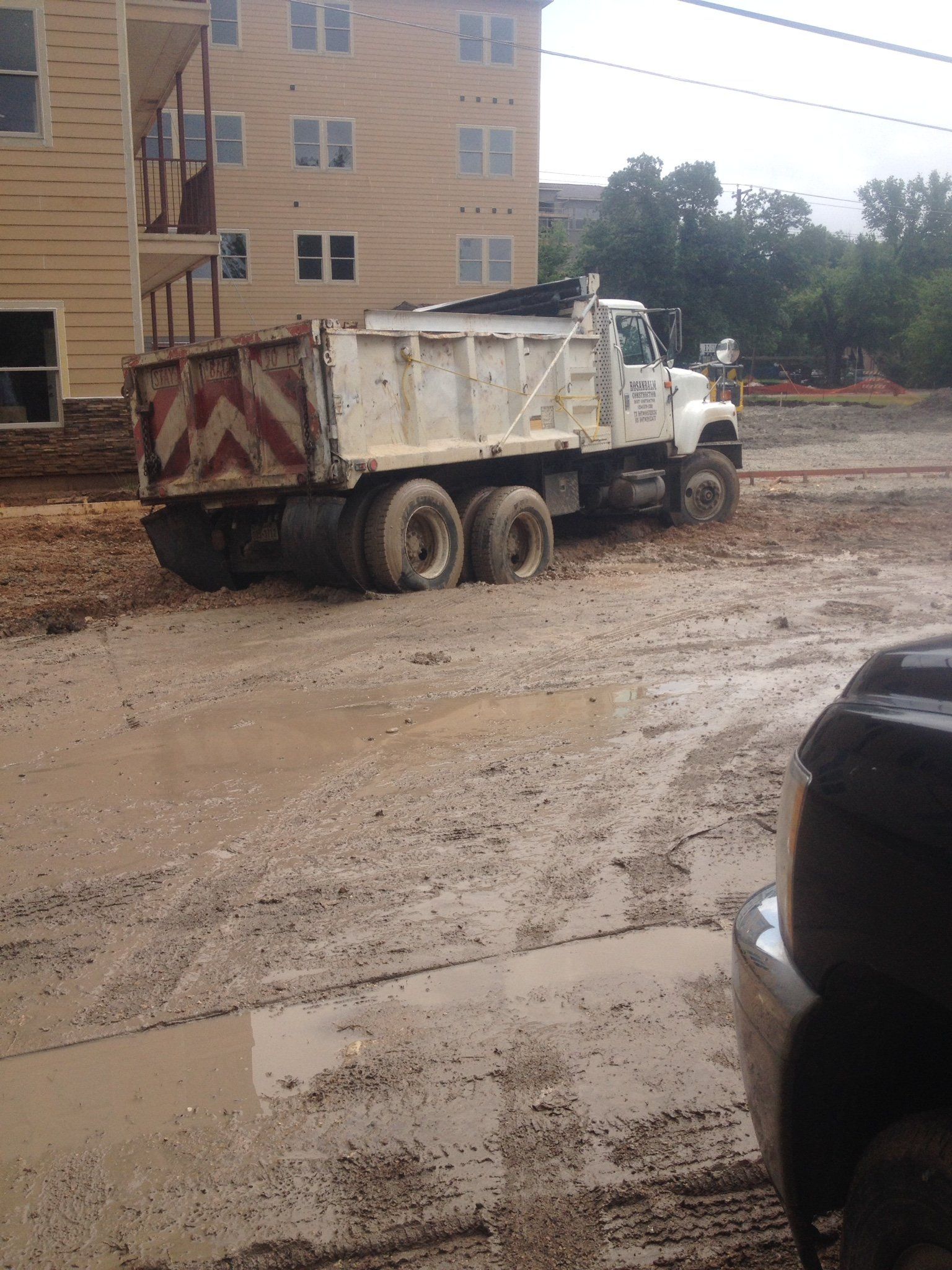White dump truck parked on a muddy construction site beside an apartment building.