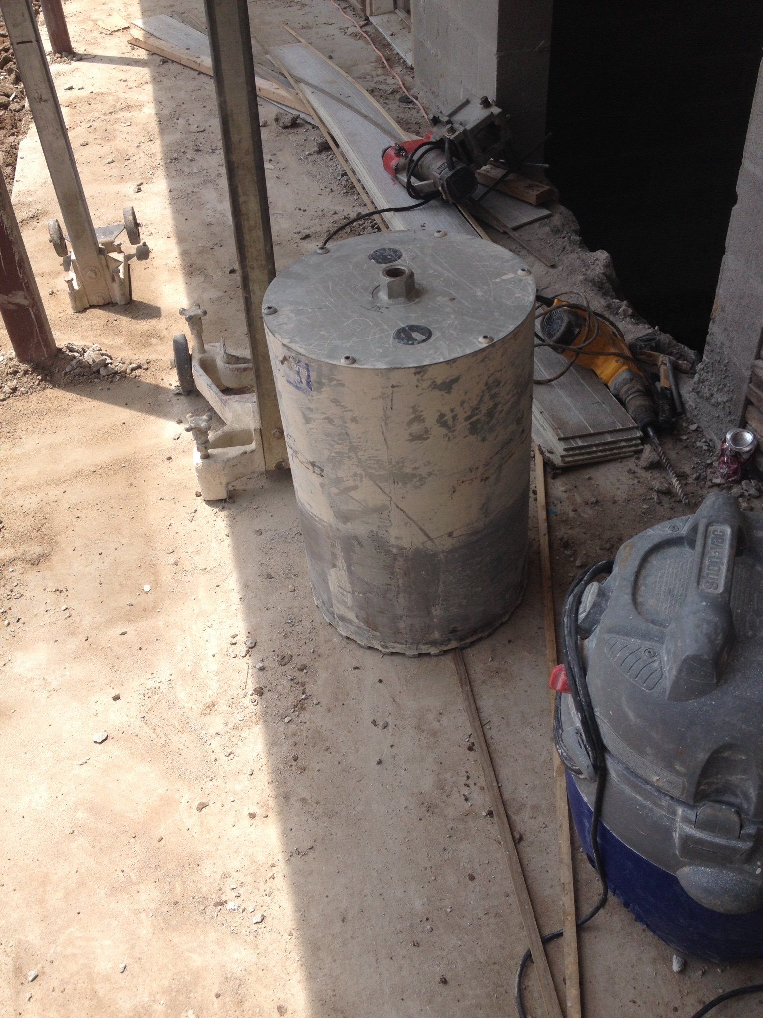 Construction site with a large cylindrical concrete post near tools and cables on a dusty floor