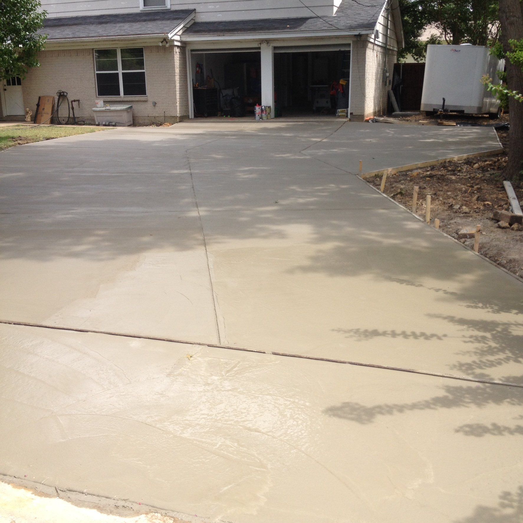 Freshly paved concrete driveway leading to a house with open garage doors and a parked trailer.