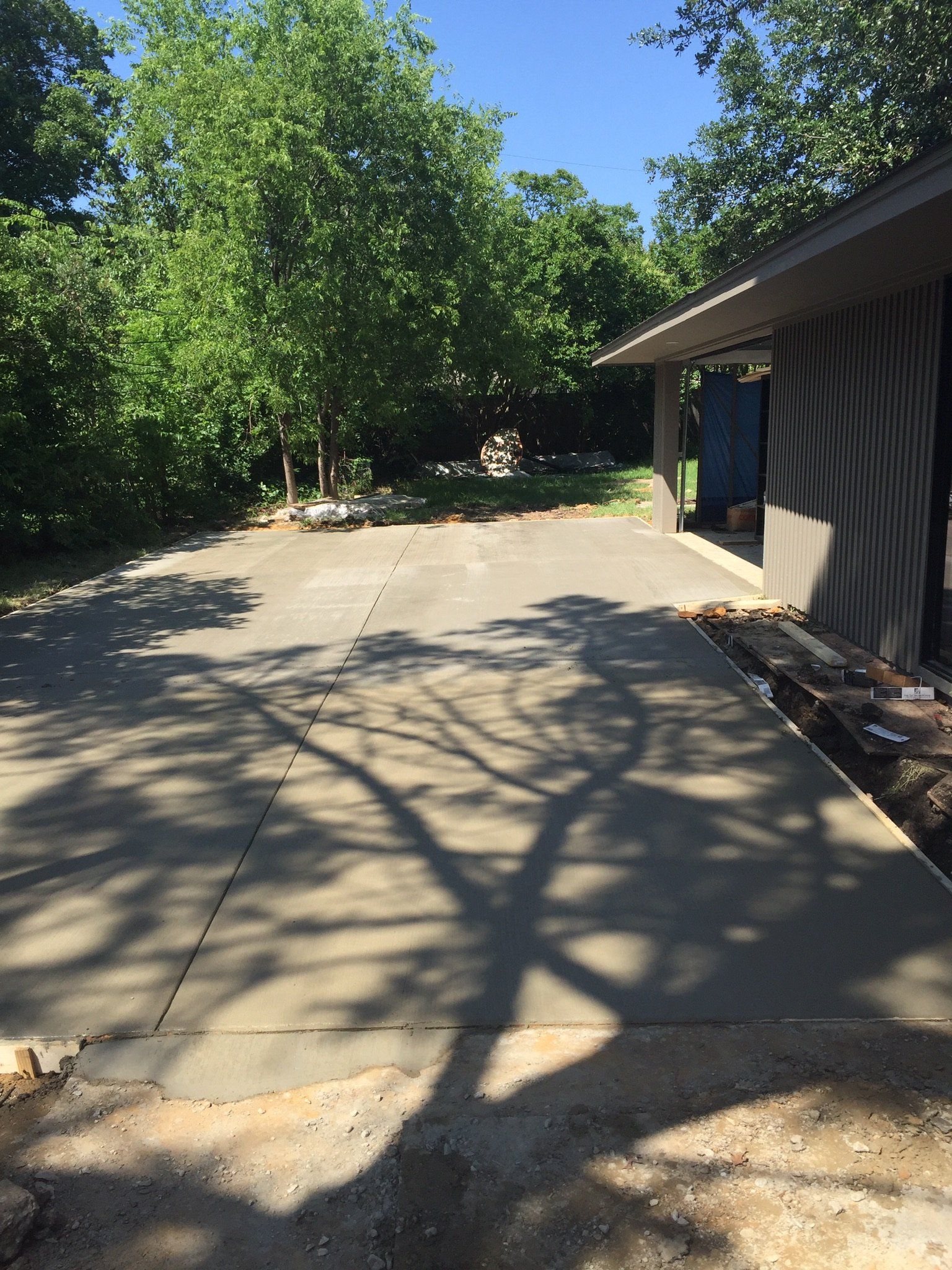Concrete driveway beside a house, shaded by trees with sunlight and long branch shadows.