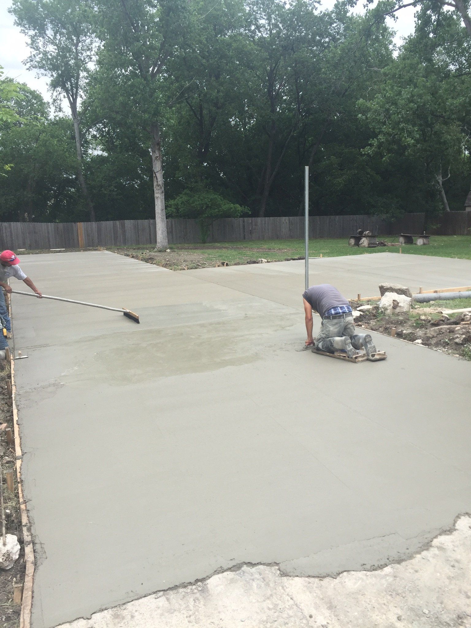 Workers smoothing wet concrete on a driveway beside a wooded area