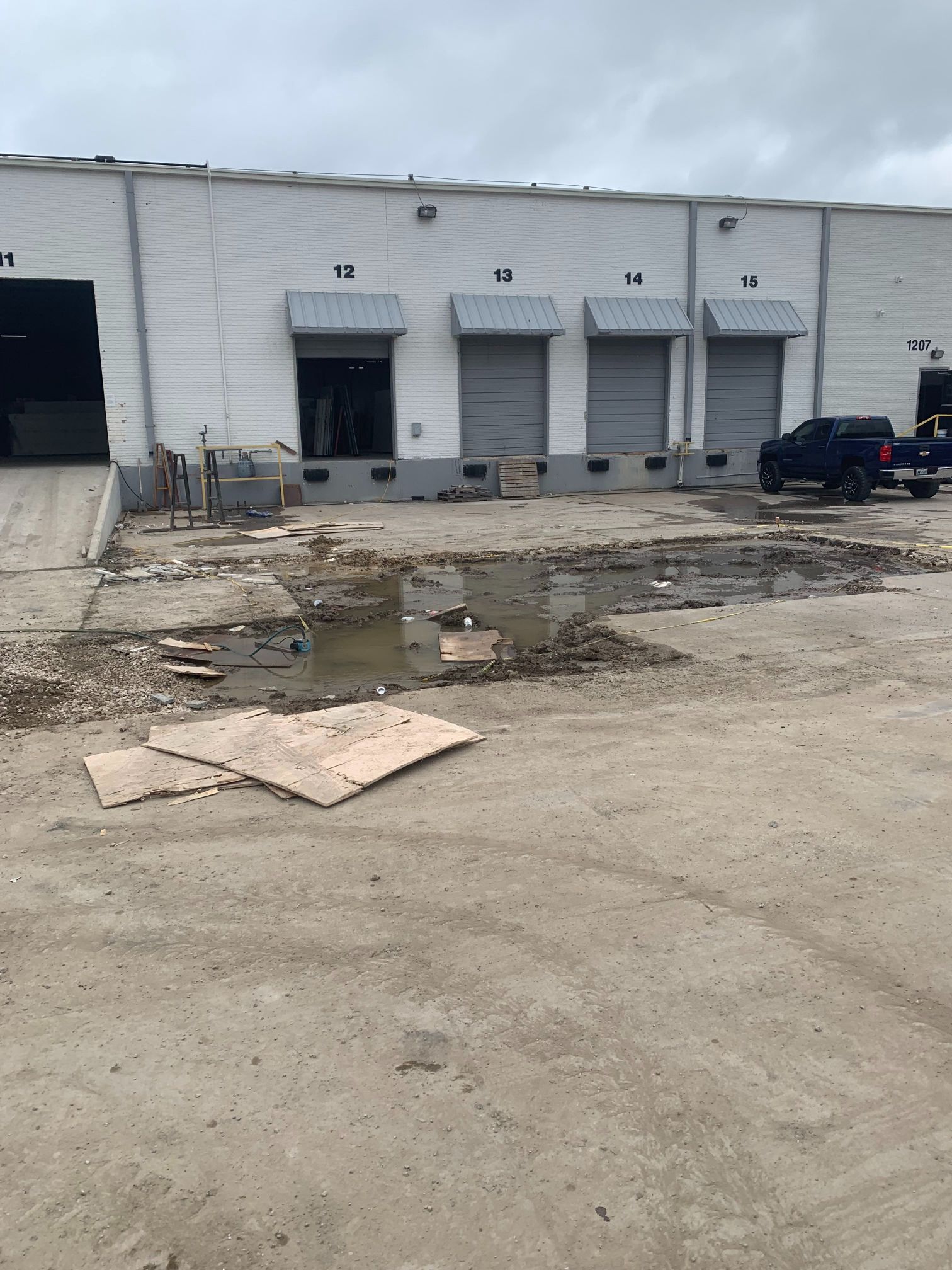 Industrial warehouse loading docks with debris-strewn pavement and a parked black SUV.