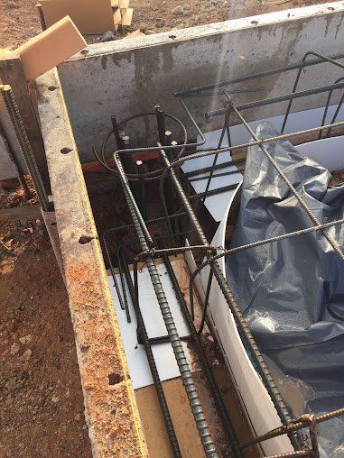 Construction pit with rebar, a black tarp, and water pooling beside concrete walls