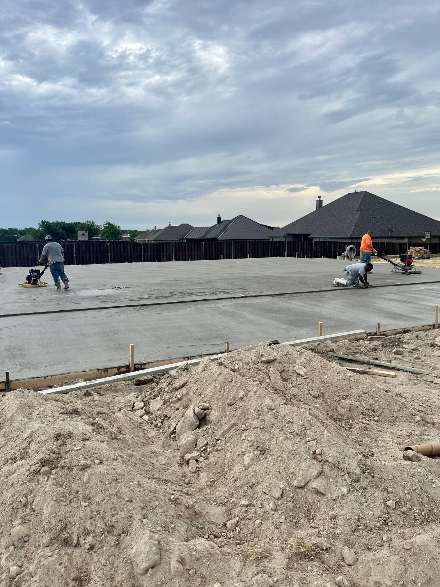 Workers smoothing fresh concrete slab at a new building site under a cloudy sky