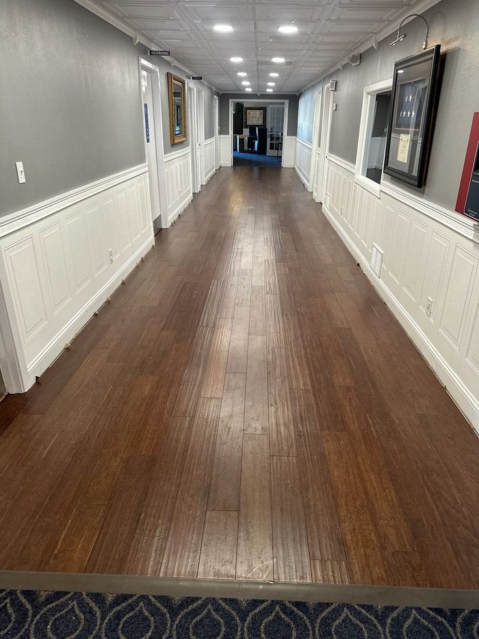 Empty hallway with wood floor, gray walls, white wainscoting, and windows on the right.