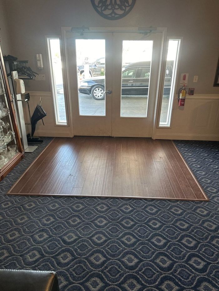 Indoor lobby with glass front doors, blue patterned carpet, and a wood mat by the entrance.