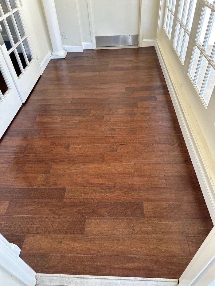 Narrow hallway with brown wood flooring, white trim, and a vent at the far end.