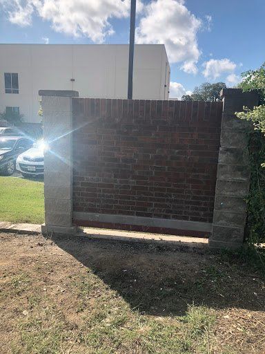 Brick sign wall with concrete pillars beside a parking lot under a partly cloudy sky