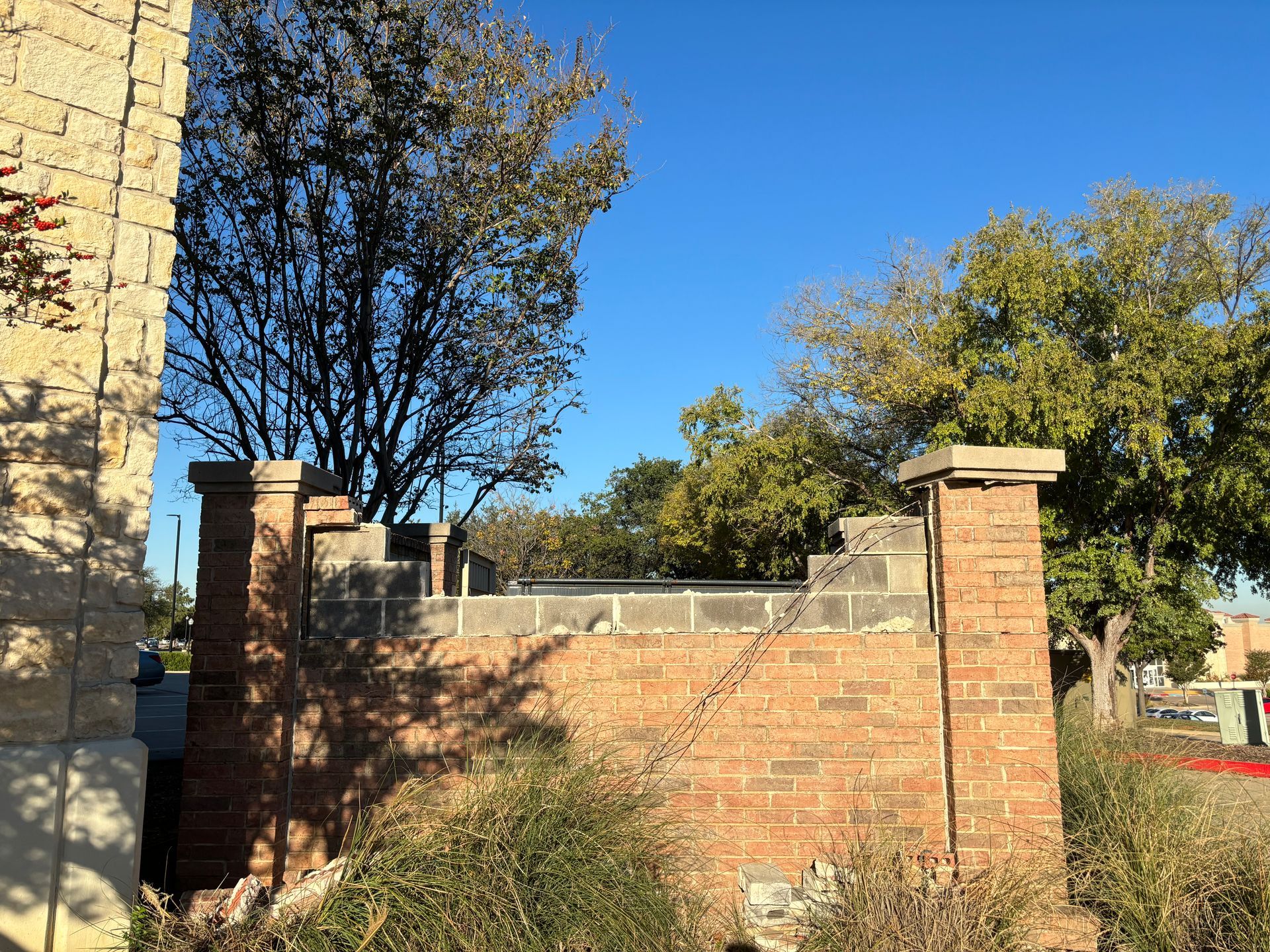 Stone wall with brick pillars beside a building, with trees and blue sky in the background