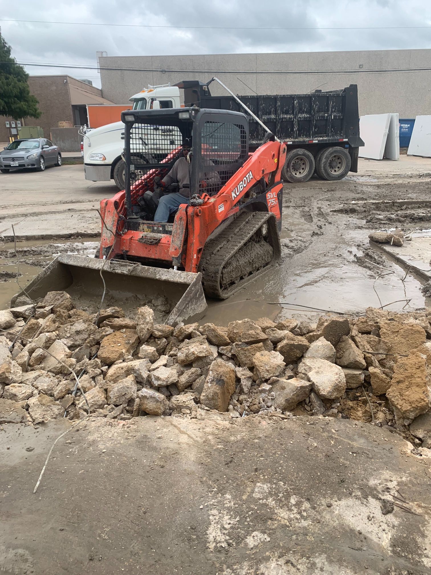 Orange skid steer moving broken concrete on a muddy construction site