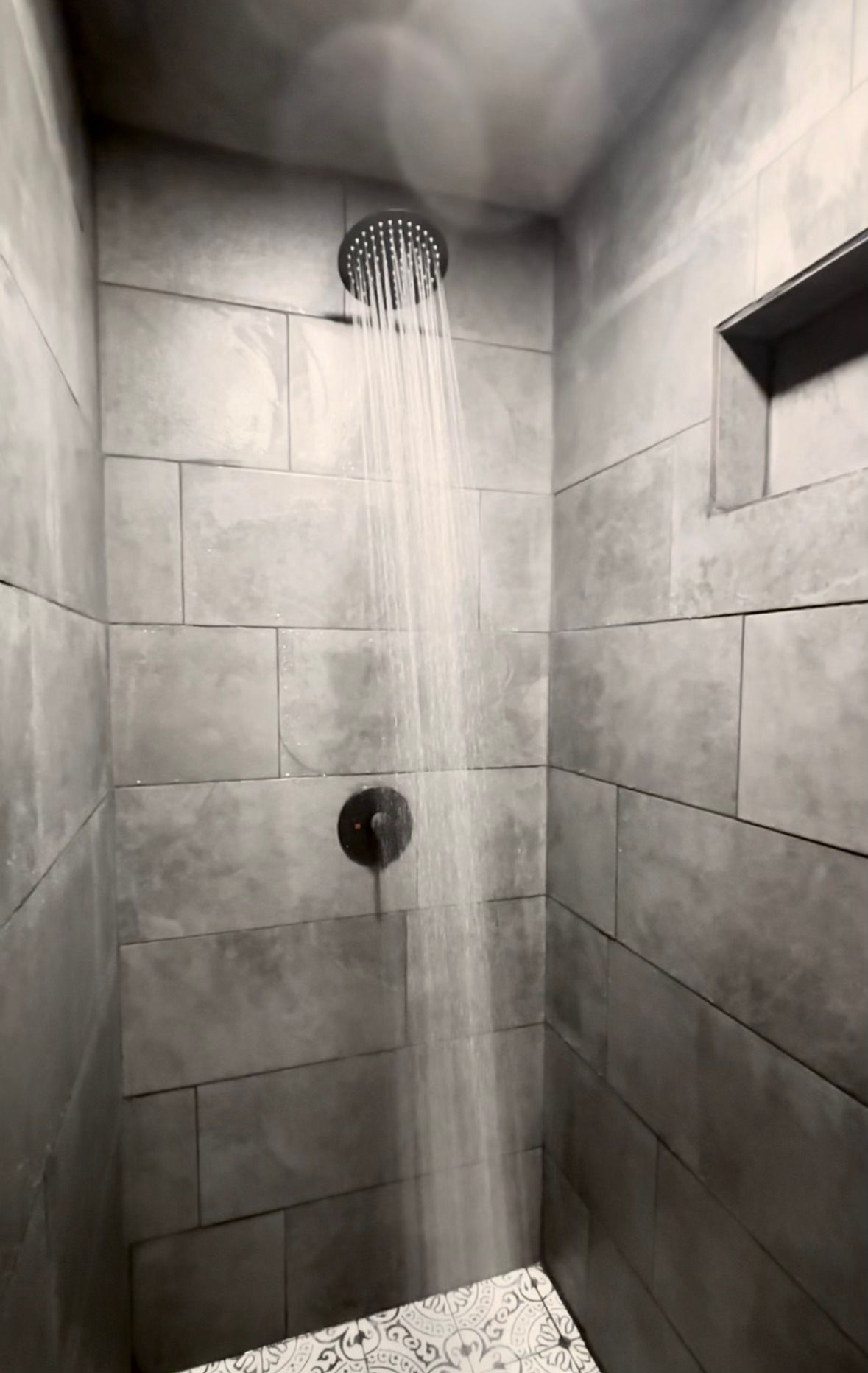 Gray tiled shower with a wall-mounted showerhead and built-in shelf.