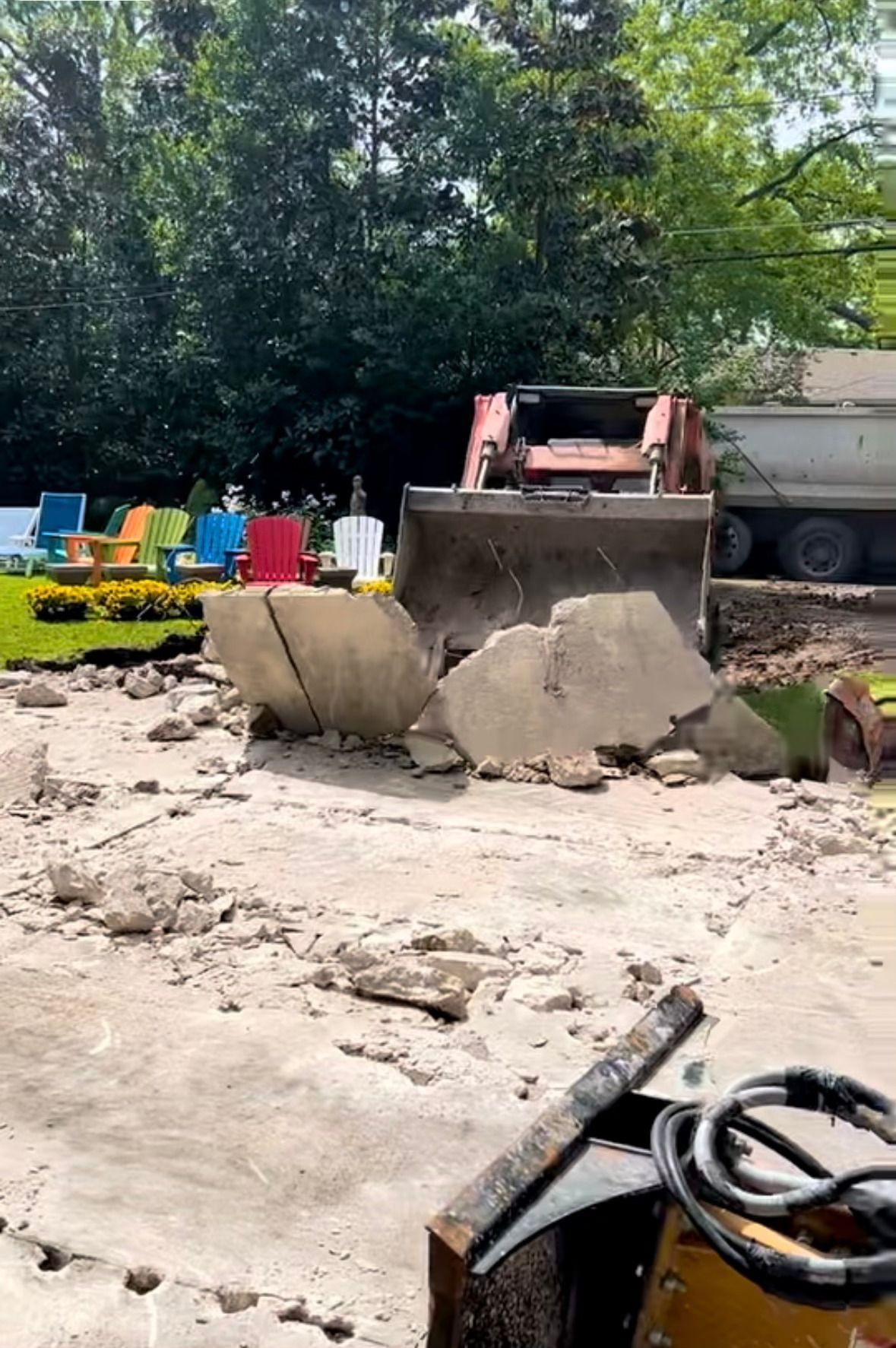 Construction site with concrete barriers, a loader, and colorful chairs under trees
