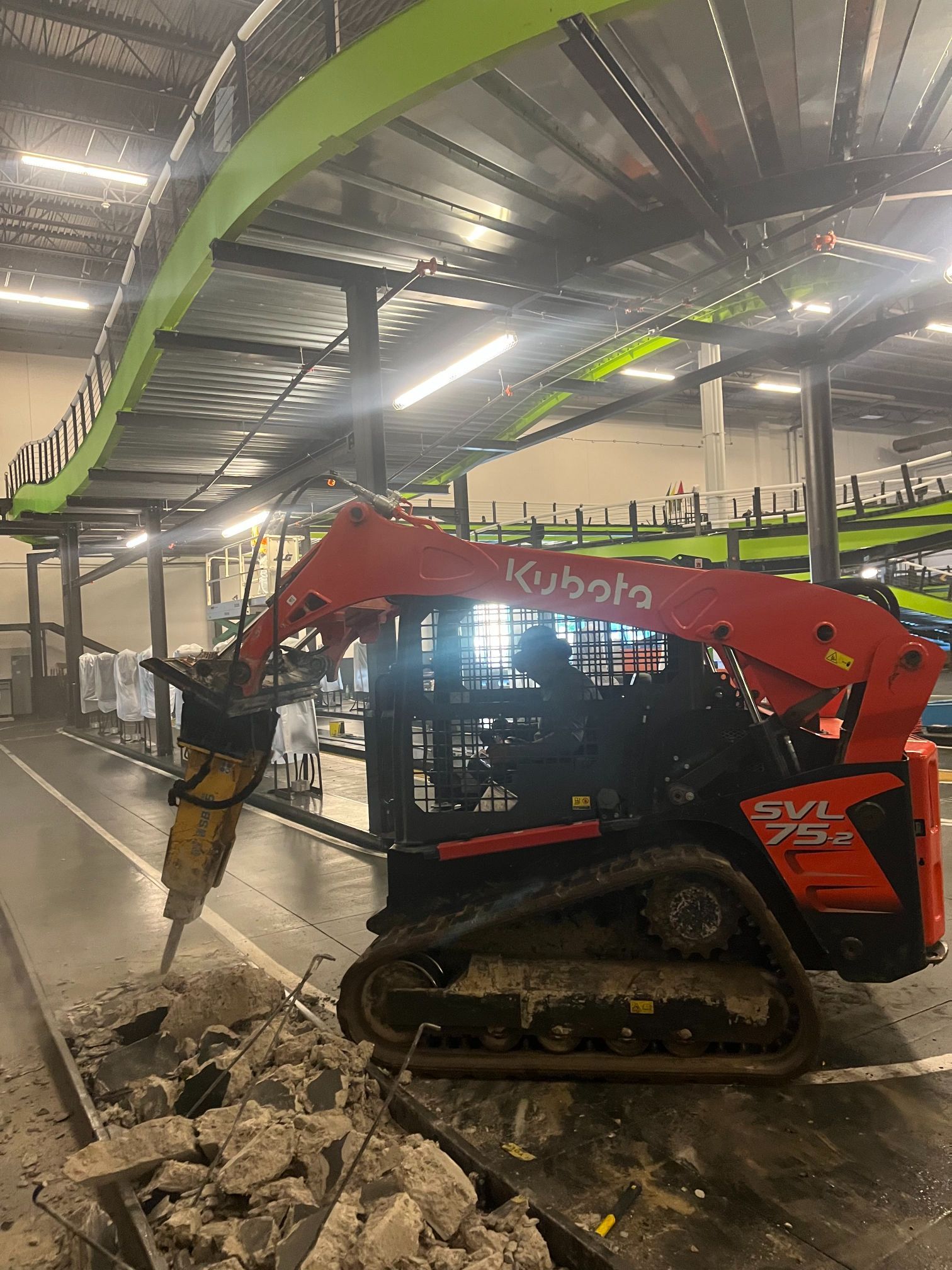 Red Kubota mini excavator breaking concrete debris inside a warehouse.
