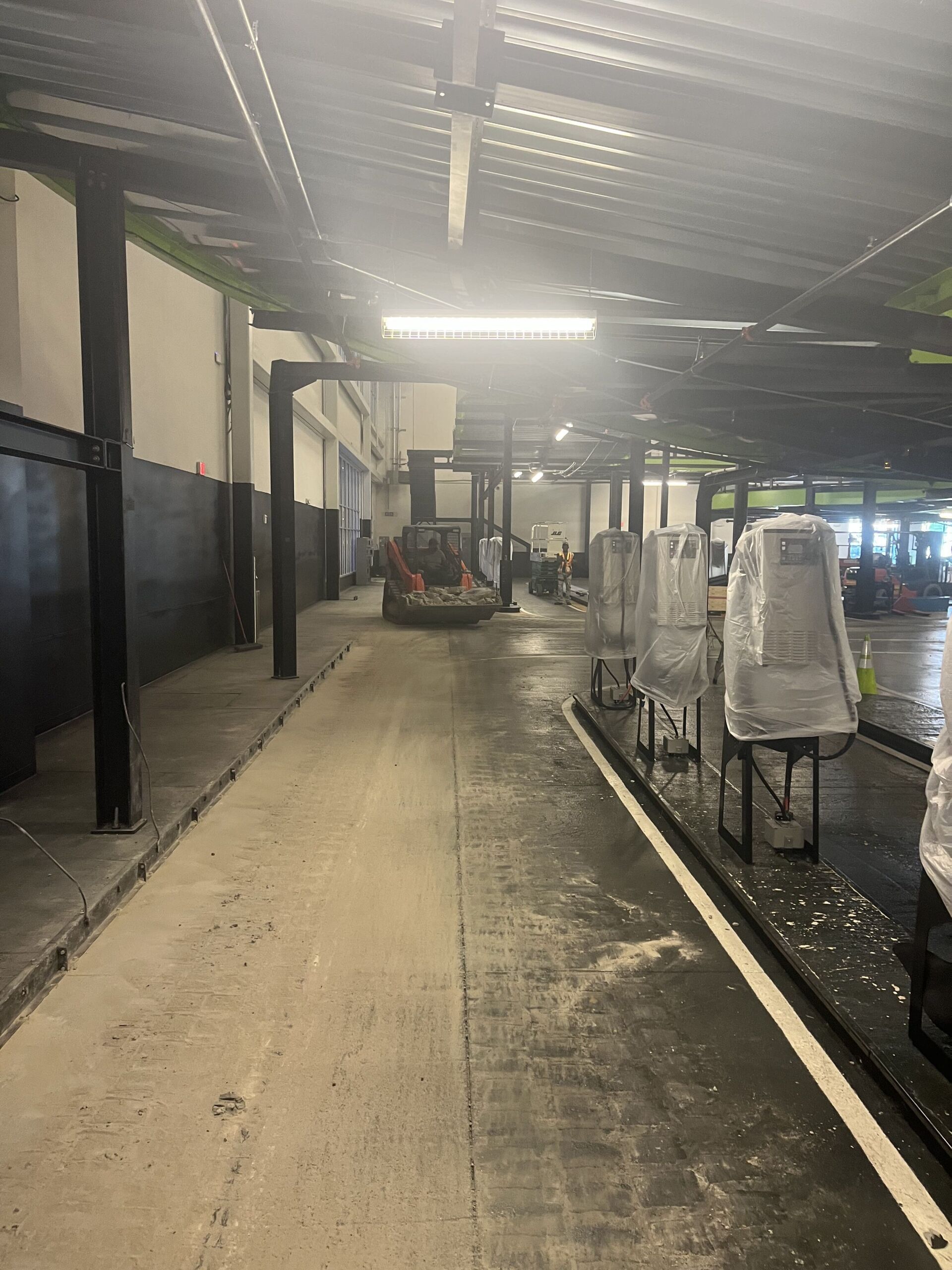 Covered walkway beside parked carts in an industrial or warehouse-style area, with wet concrete floor and overhead lights