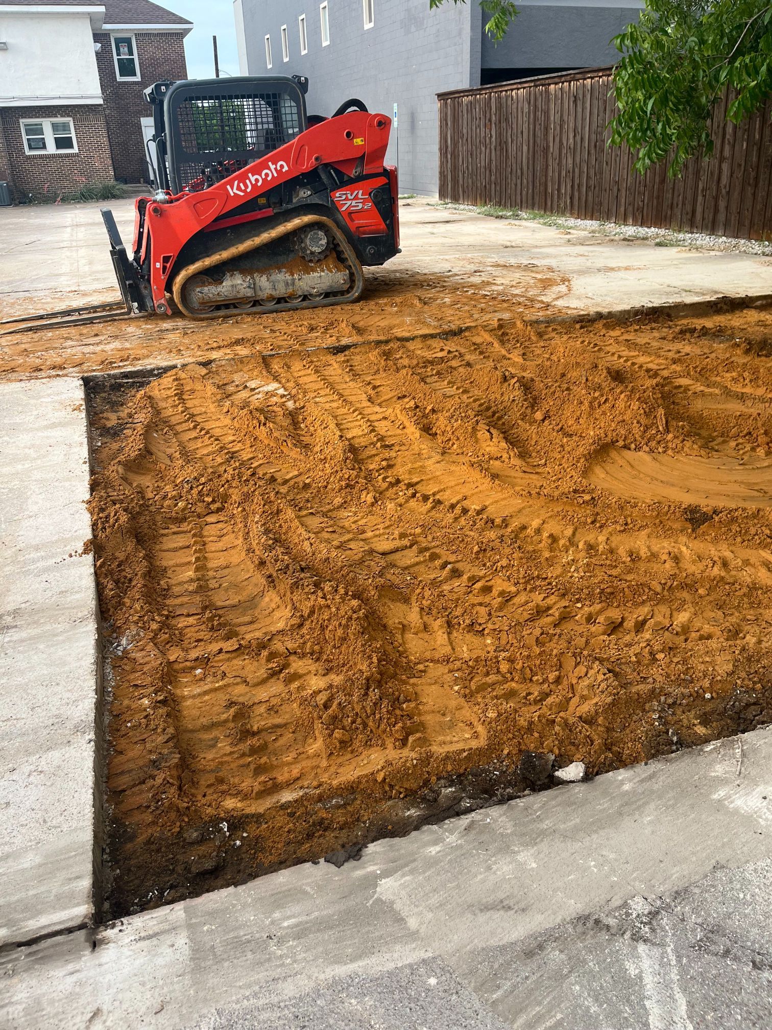 Red skid steer grading a muddy construction lot beside a driveway and houses