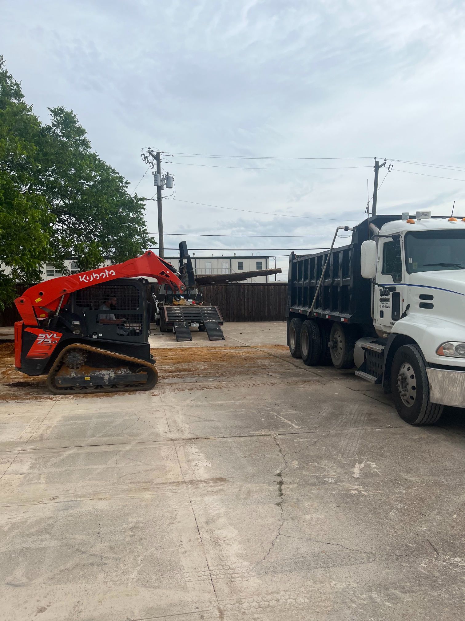 Red excavator beside white dump truck in a gravel lot under cloudy sky