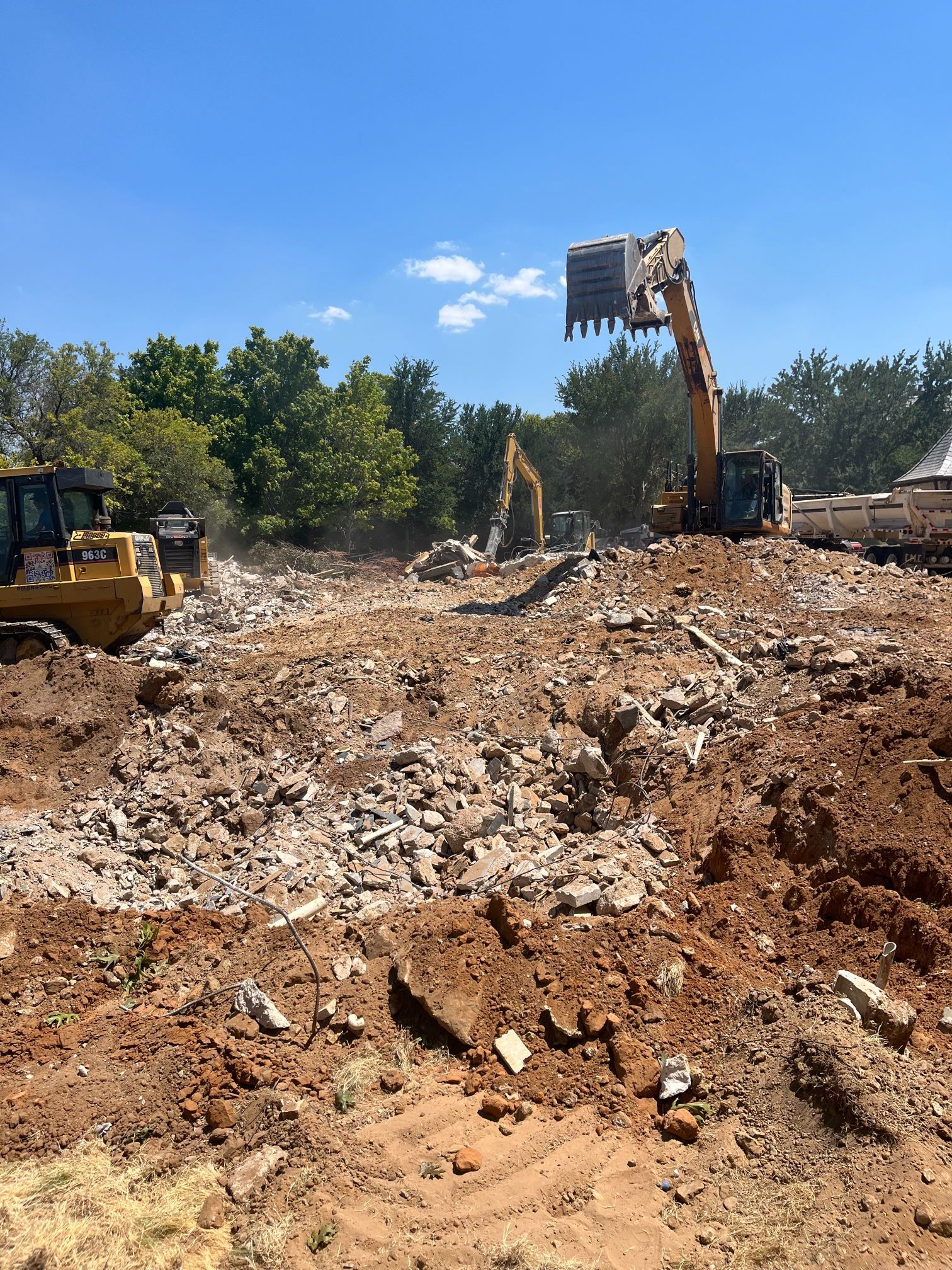 Excavators and a bulldozer at a dusty construction site under a clear blue sky