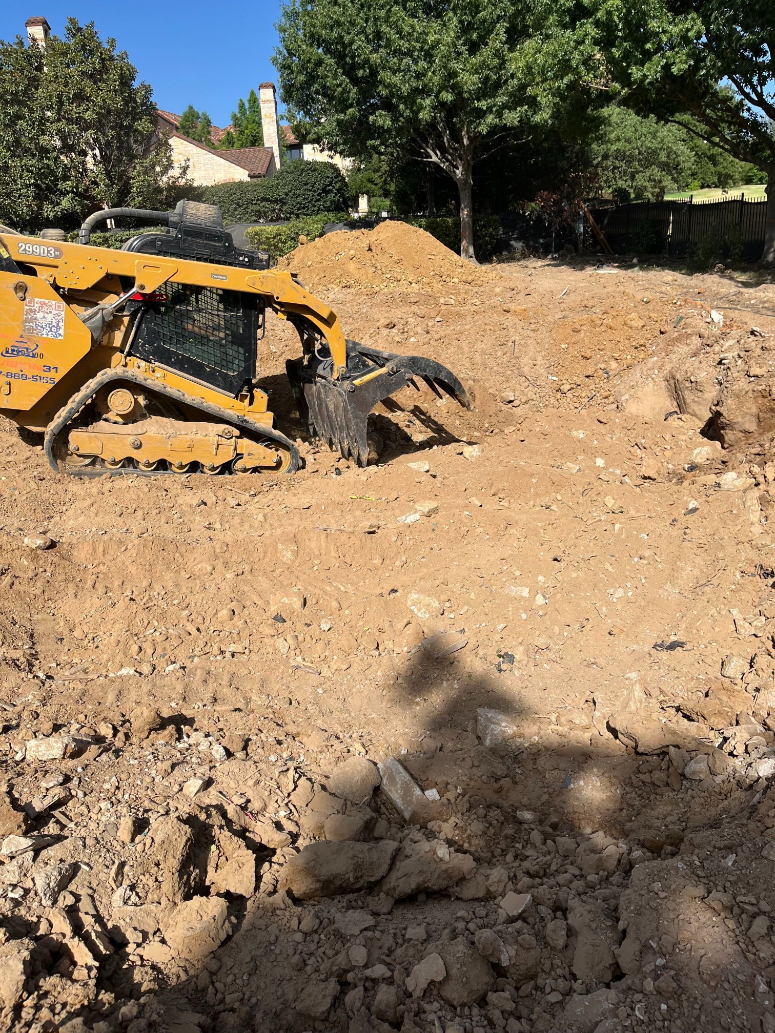Yellow mini excavator digging in a dirt lot near trees and houses