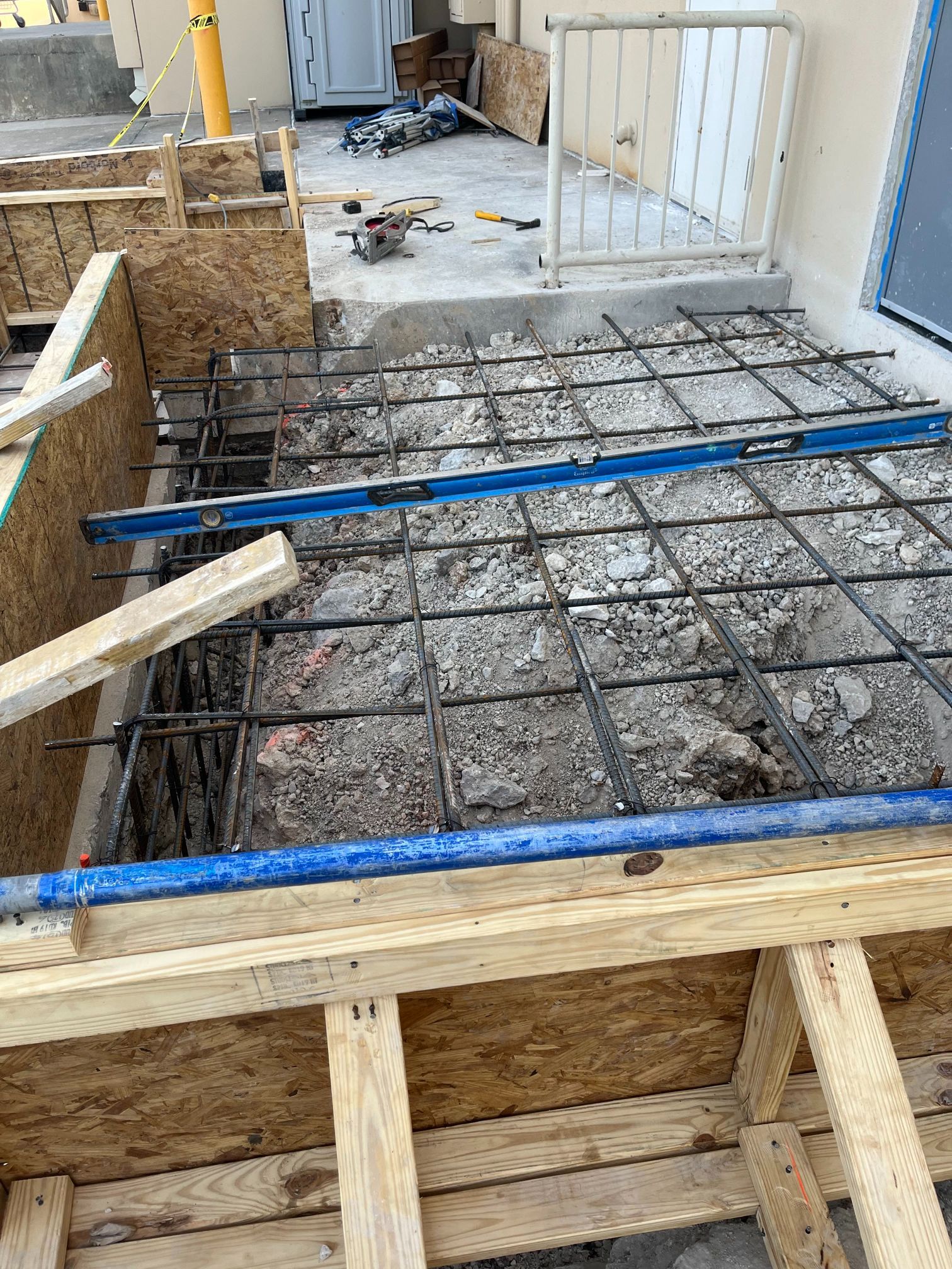 Construction site with steel rebar grid over a concrete slab and wooden formwork around the edges