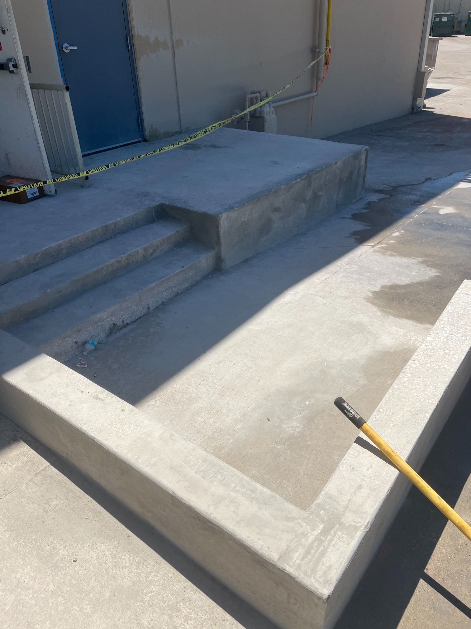Concrete accessibility ramp and steps beside a blue door, with yellow caution tape across the entrance.