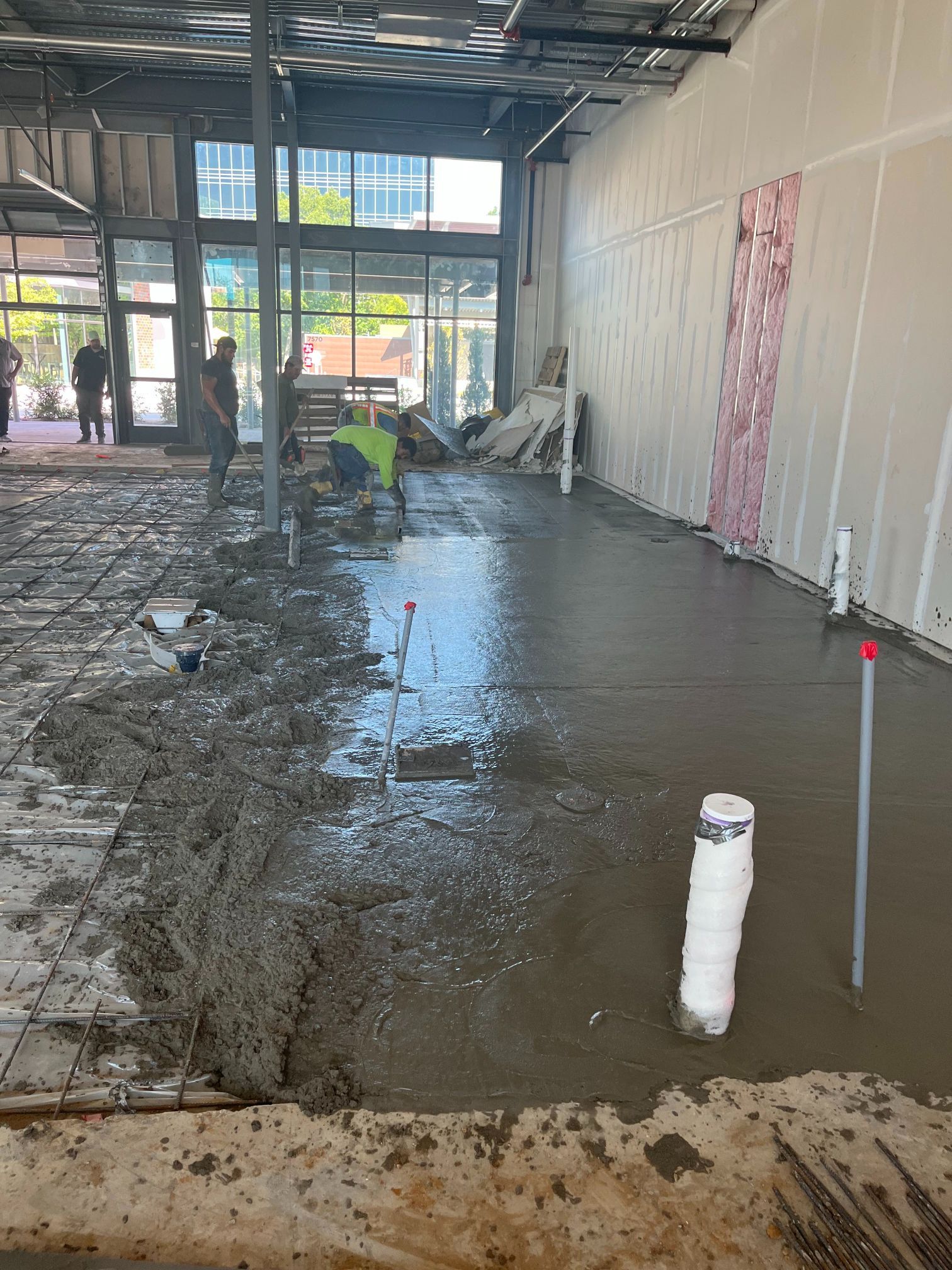 Flooded indoor construction area with wet concrete, standing water, and workers in the background