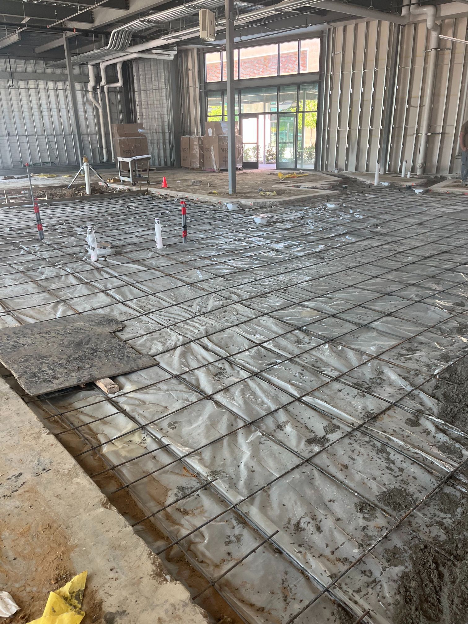 Interior construction site with rebar grid over plastic sheeting on a concrete floor.