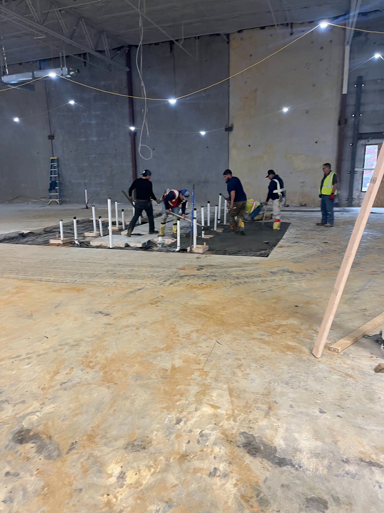 Construction workers pouring concrete on a slab inside an unfinished warehouse.