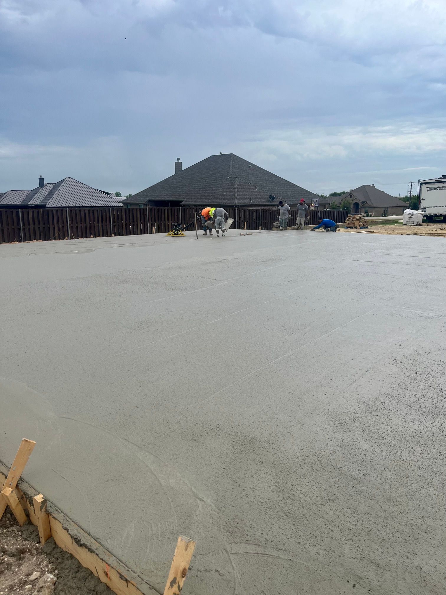 Fresh concrete slab at a construction site with workers and houses under a cloudy sky