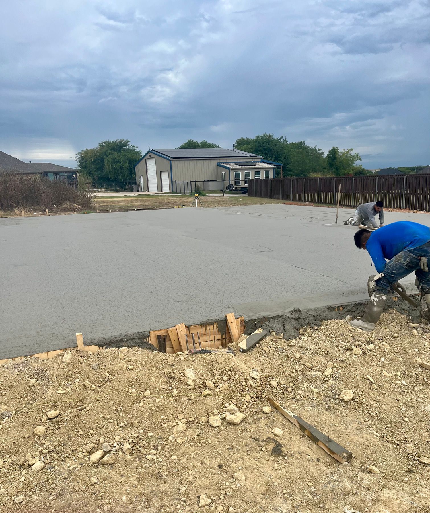 Worker smoothing fresh concrete on a residential driveway under cloudy sky