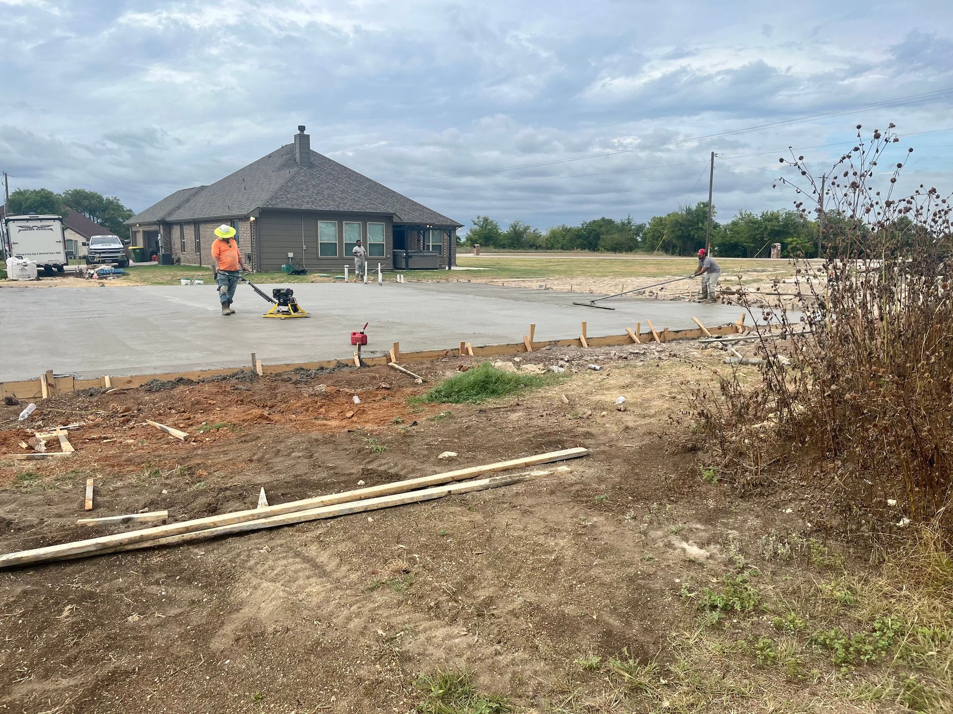 Construction worker grading a lot beside a gray house under a cloudy sky