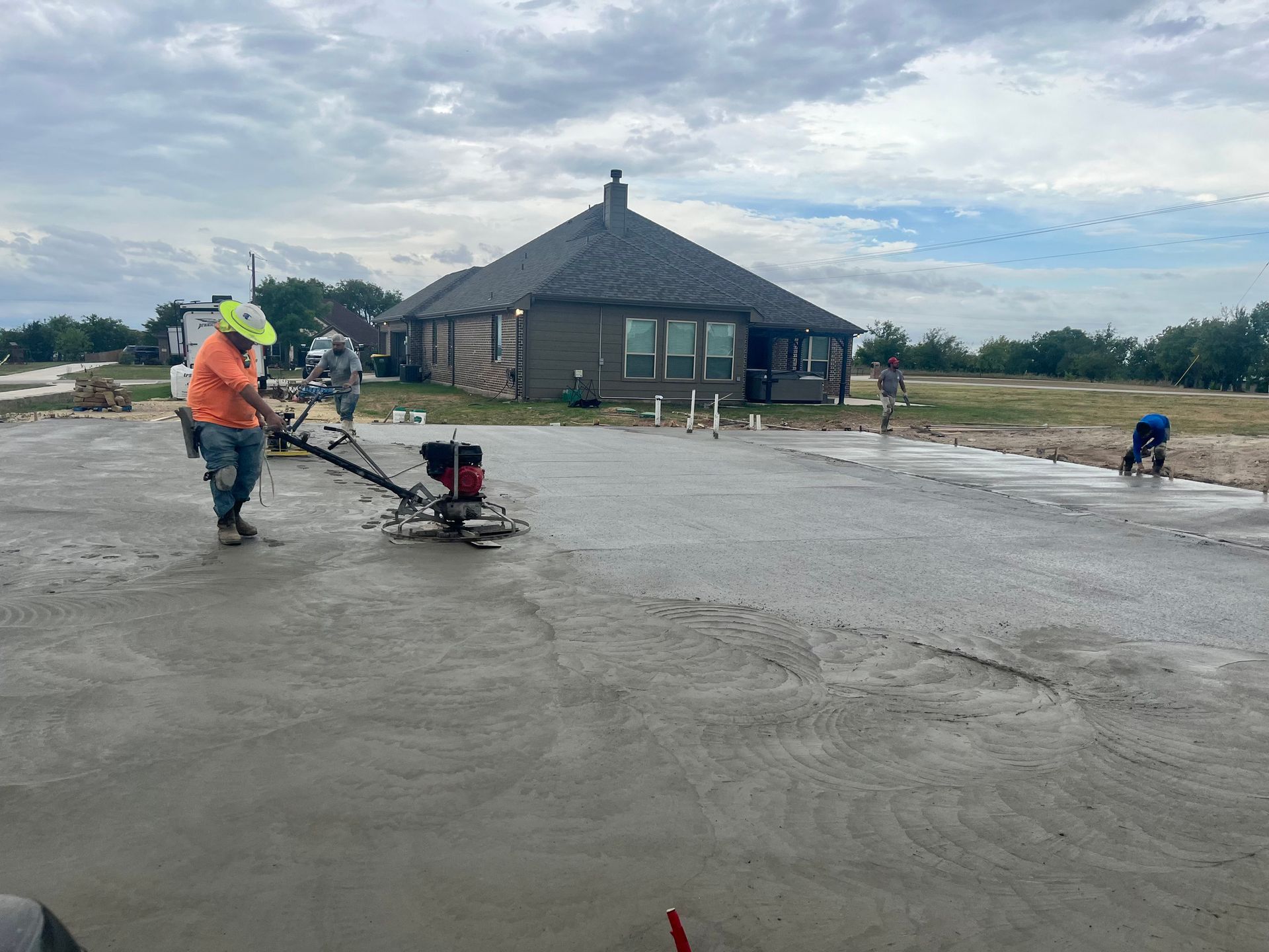 Workers smoothing fresh concrete outside a dark gray house on a cloudy day