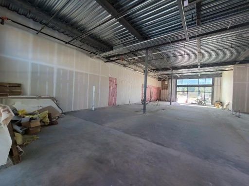Empty unfinished warehouse with concrete floor, exposed ceiling beams, and stacked materials along the left wall