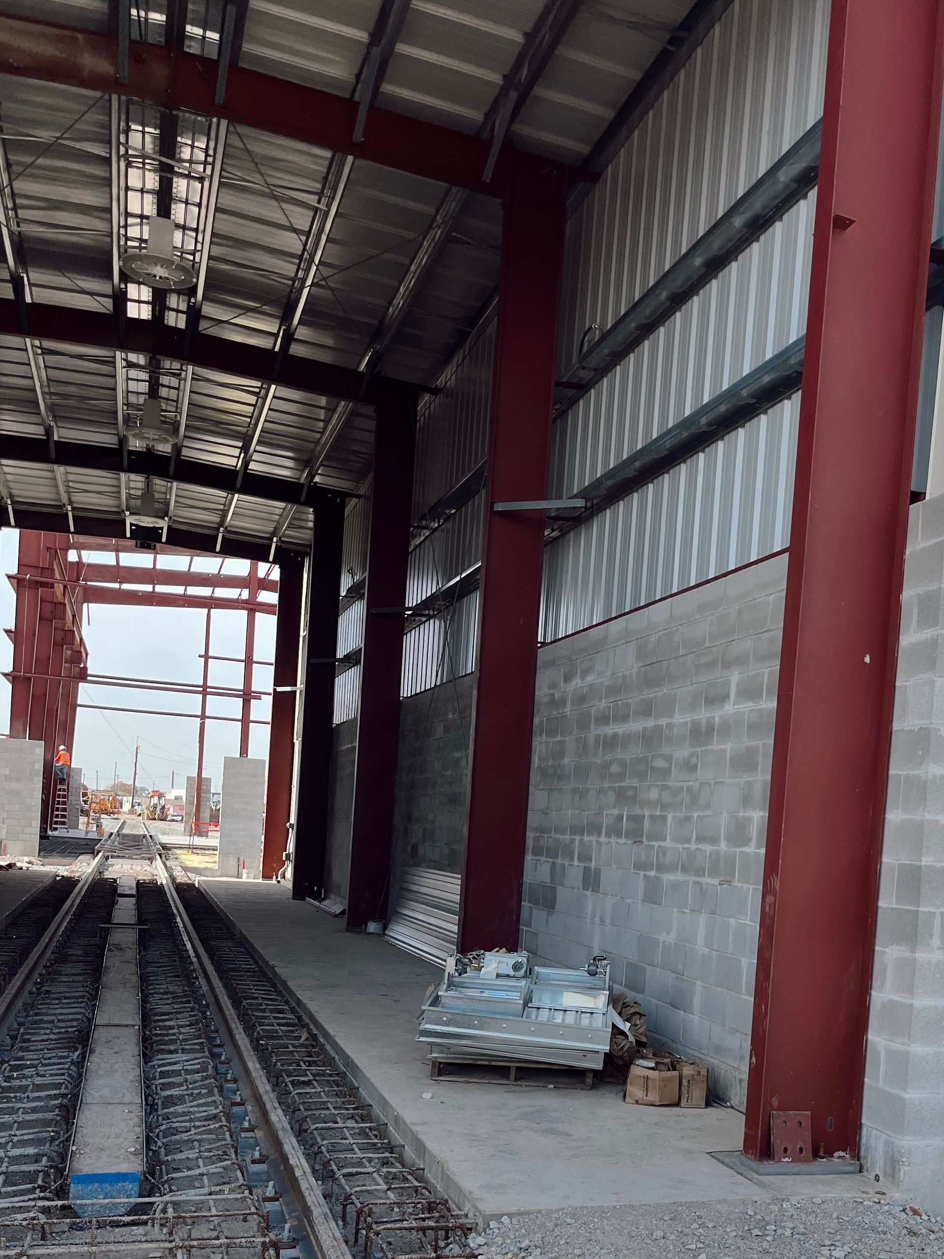 Red steel-framed industrial corridor with train tracks and concrete walls under construction
