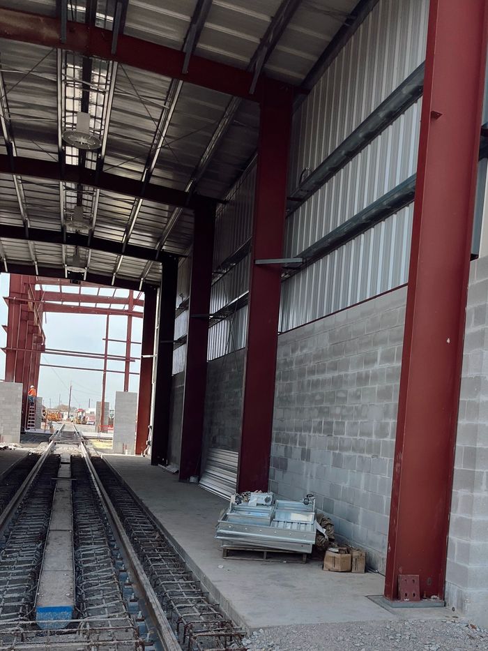 Rail tracks inside an unfinished industrial building with red steel columns and corrugated metal walls
