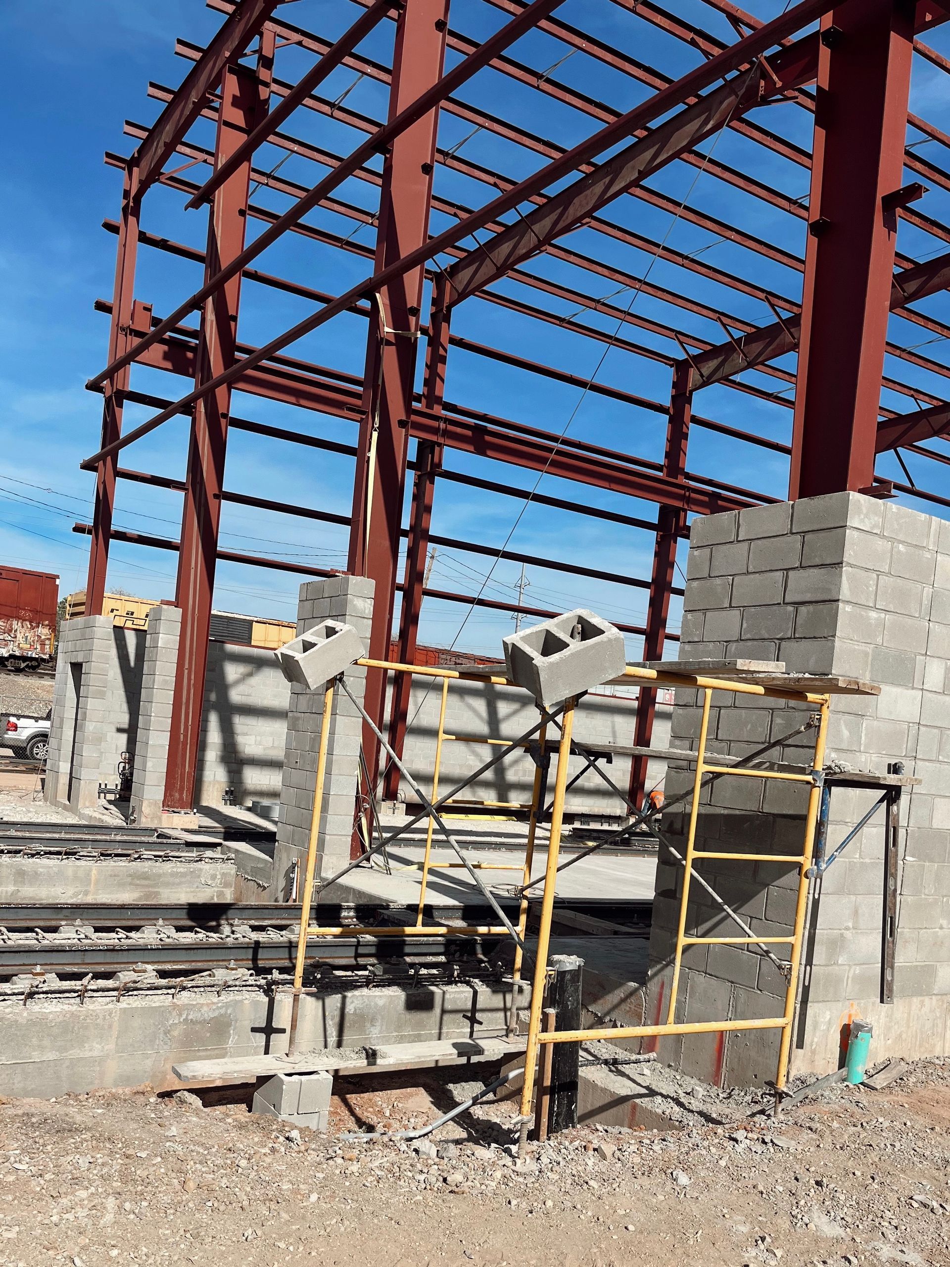 Steel frame building under construction with scaffolding and cinder block walls on a gravel lot