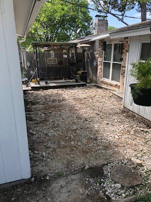 Narrow gravel side yard between houses with a small fenced deck and screened porch in the background