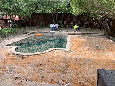 Backyard pool being cleaned, with two workers by a fenced, tree-lined patio area