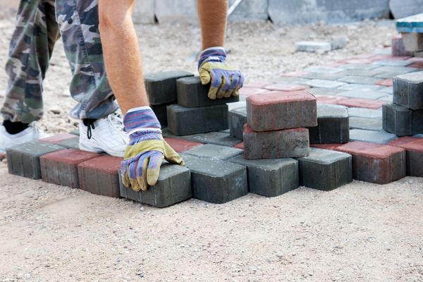 Worker laying gray and red paving blocks on a sandy ground surface